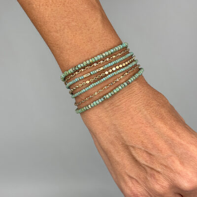 Gros plan sur un bracelet manchette, doré, avec perles de verre turquoises, porté au poignet d'un modèle.