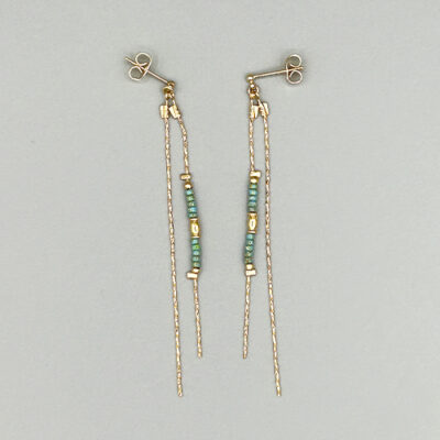 Detail boucles d'oreilles dorées à l'or 18 carats avec perles de verre japonaises turquoises et maille serpent. Packshot sur fond gris.