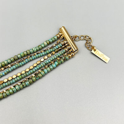 Détail rallonge et tag bracelet manchette dorée a l'or 18 carats avec perles de verre japonaises turquoises. Packshot sur fond gris.